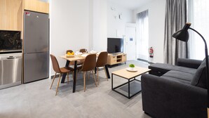 Een moderne keuken met een ingebouwde vaatwasser en koelkast, een eethoek met een tafel en stoelen, een grijze bank en een kleine salontafel.