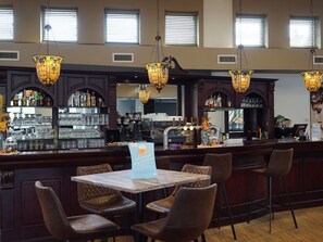A bar area with a counter, bar stools, and hanging lamps. There are shelves with bottles and glasses behind the counter.