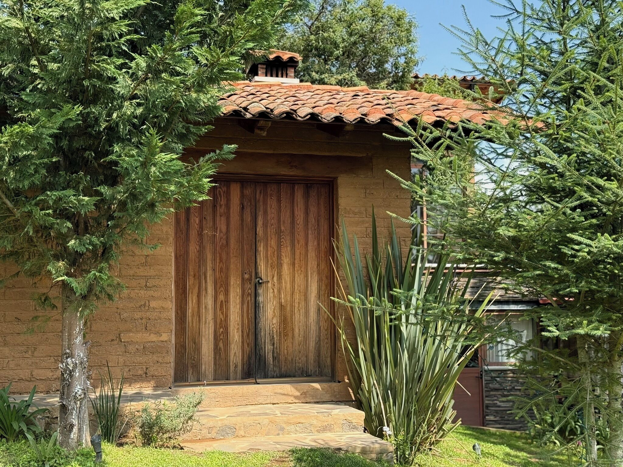 A rustic building with a wooden door, a tiled roof, and a stone pathway leading to the entrance.