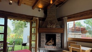 A cozy room with a stone fireplace, wooden furniture, and large windows offering a view of the outdoors. - Cabañas Santa Fe Tapalpa (Tapalpa)