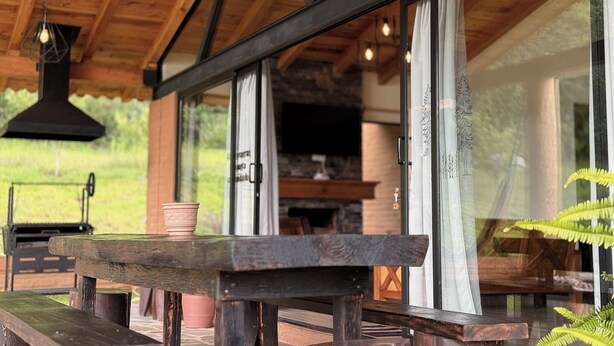 An outdoor wooden deck with a rustic bench and a table, large windows, and a stone fireplace visible inside. - Cabañas Santa Fe Tapalpa (Tapalpa)