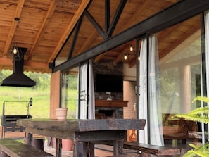 An outdoor wooden deck with a rustic bench and a table, large windows, and a stone fireplace visible inside. - Cabañas Santa Fe Tapalpa (Tapalpa)