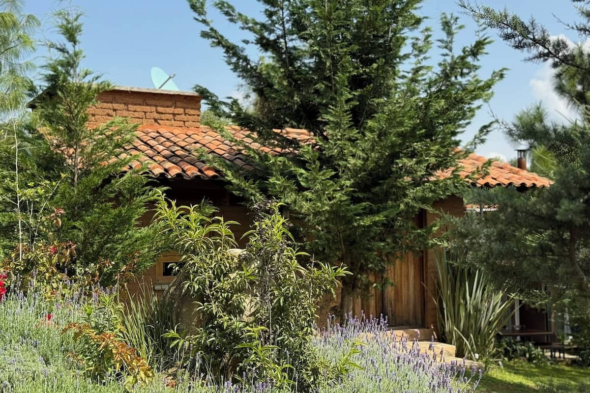 Un bâtiment rustique, doté d’un toit en tuiles, entouré d’une végétation luxuriante et de plantes en fleurs.