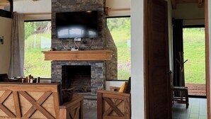 A cozy living area with a stone fireplace, wooden furniture, and a large TV mounted on the wall. - Cabañas Santa Fe Tapalpa (Tapalpa)