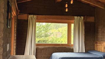 Una habitación rústica con dos camas, una ventana con cortinas, vigas de madera y lámparas colgantes.