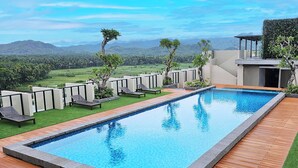 Una piscina rectangular con muelle de madera y sillas de descanso, rodeada por un jardín ajardinado y vistas a montañas lejanas.