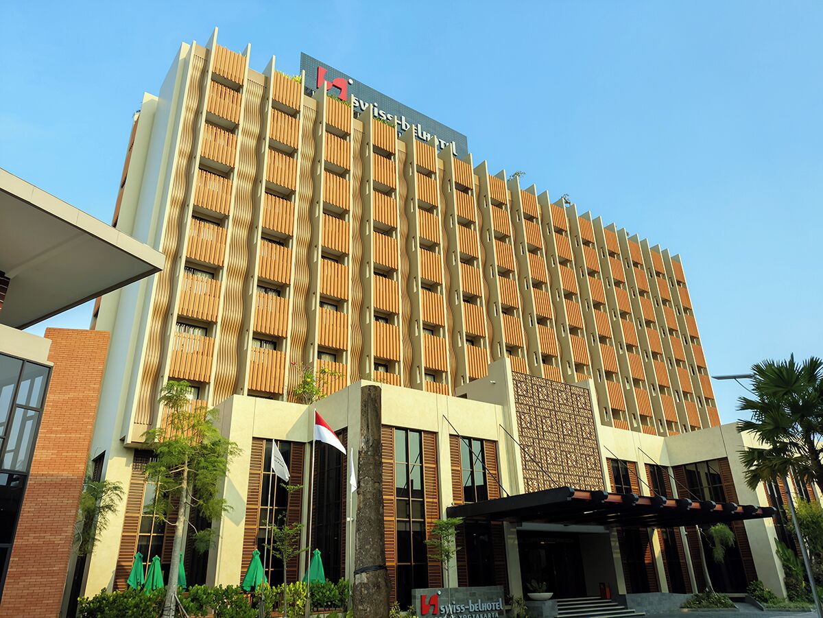 A modern hotel with a distinctive wavy facade, multiple balconies, and a prominent Swiss logo.