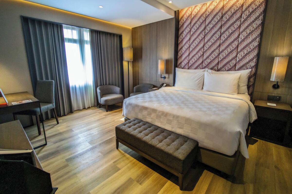 Quarto de hotel moderno com uma cama grande, uma escrivaninha, uma cadeira e um banquinho.