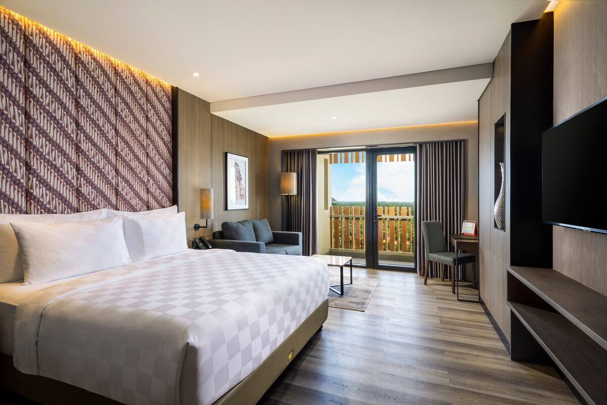 Quarto de hotel moderno com uma cama grande, uma escrivaninha, uma cadeira e uma televisão.