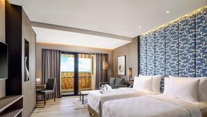 Habitación de hotel con dos camas, televisión, escritorio y balcón con vistas.