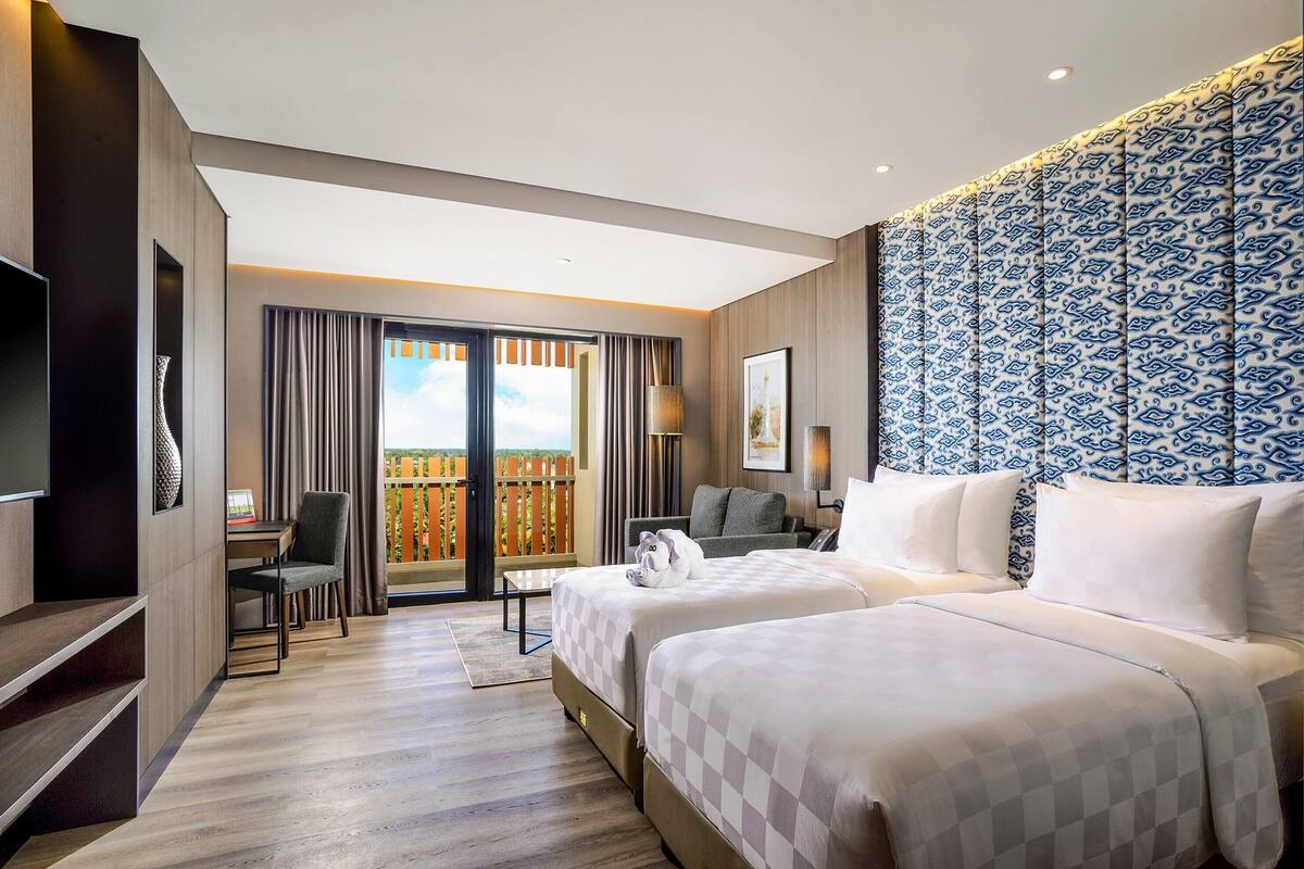 Quarto de hotel com duas camas, televisão, escrivaninha e varanda com vista.
