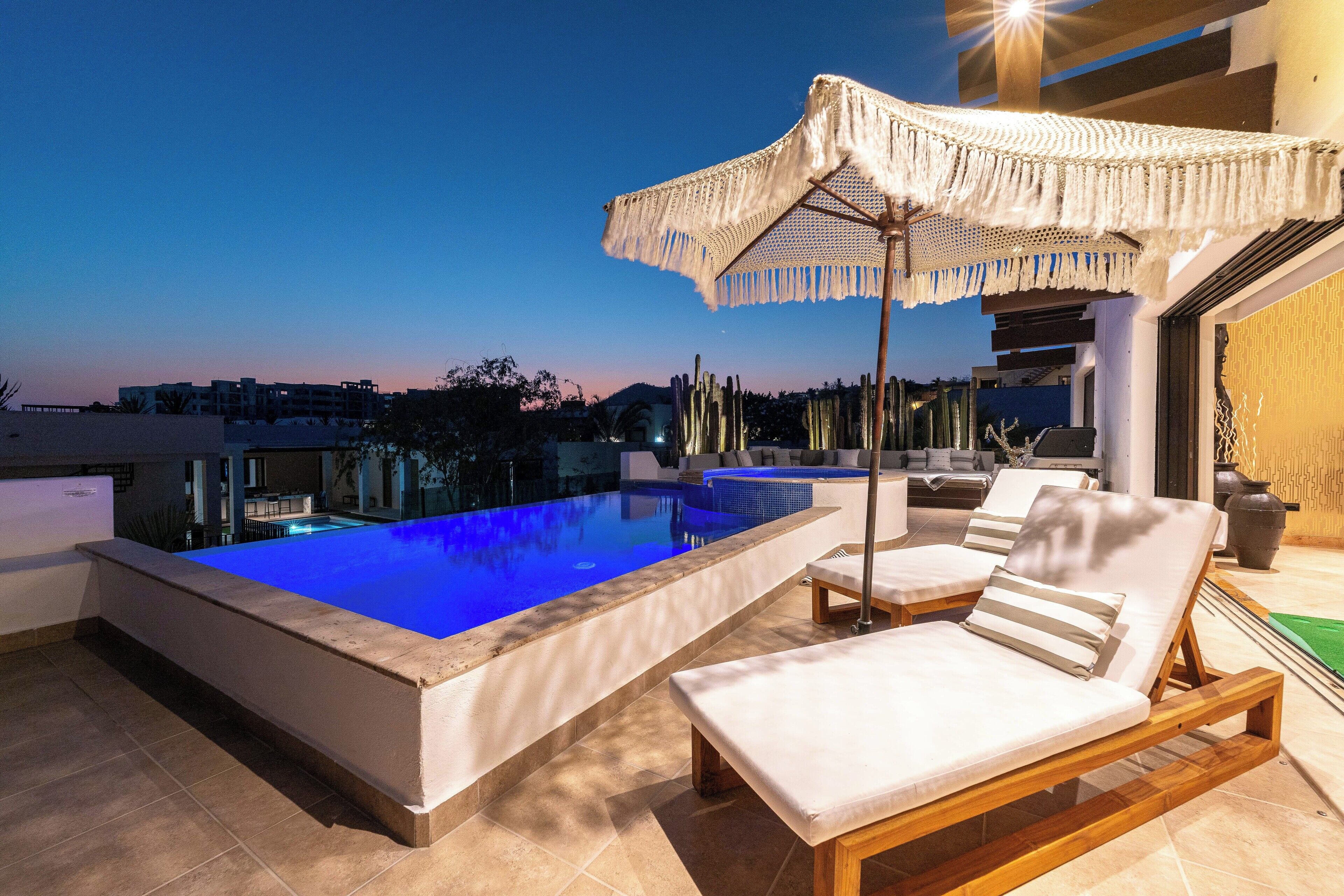 A rooftop pool area with a clear blue pool, lounge chairs, and a decorative umbrella.