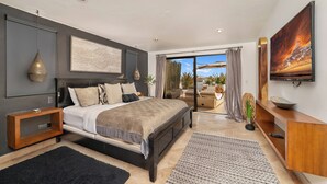 A modern bedroom with a large bed, a TV, and a balcony with a view. - Villa Cactus (Cabo San Lucas)