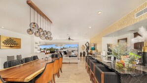 A spacious dining area with a long wooden table, black chairs, and hanging light fixtures. - Villa Cactus (Cabo San Lucas)