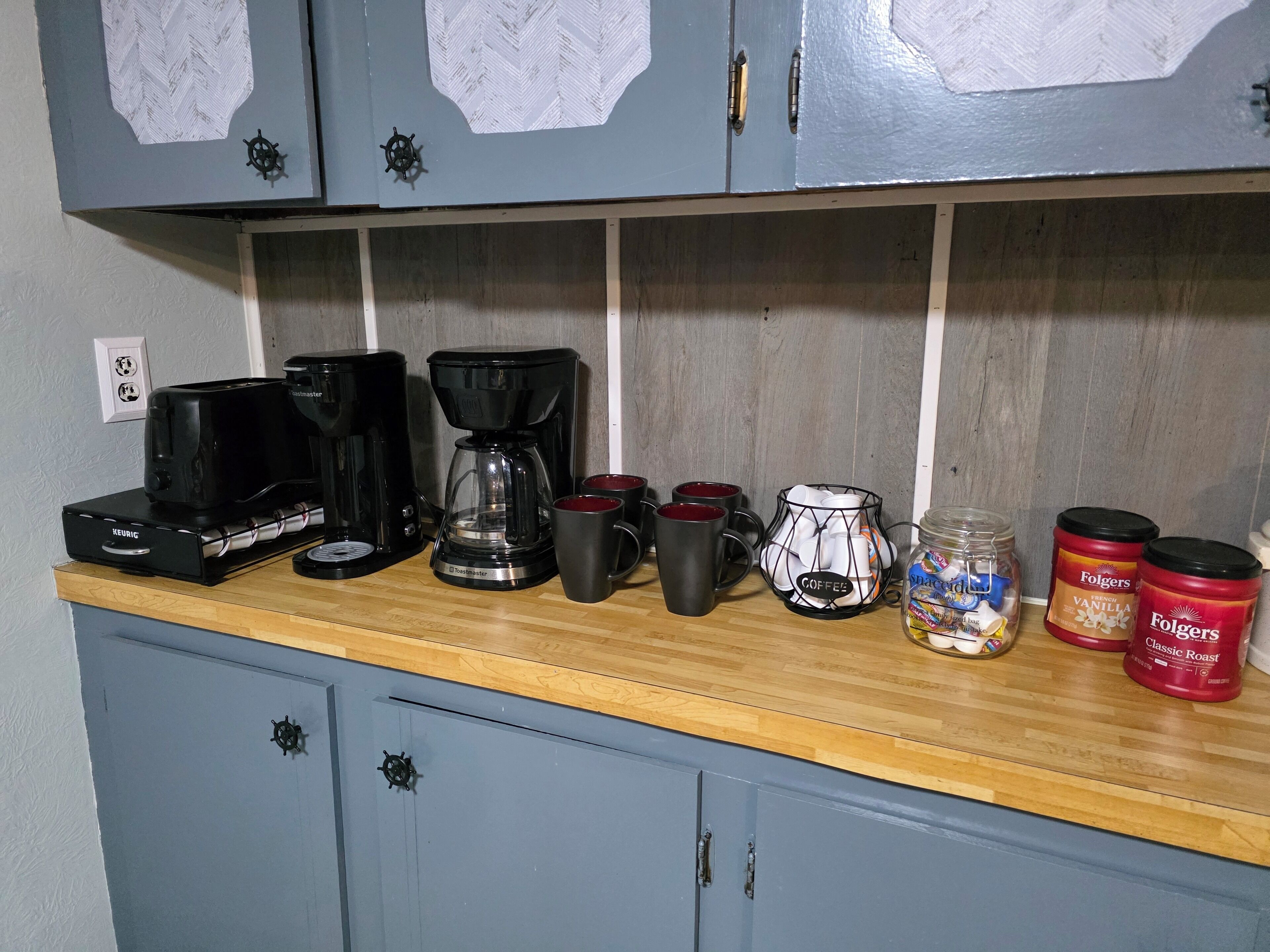 Et køkken med kaffemaskine, krus og kaffebægre på bordet.