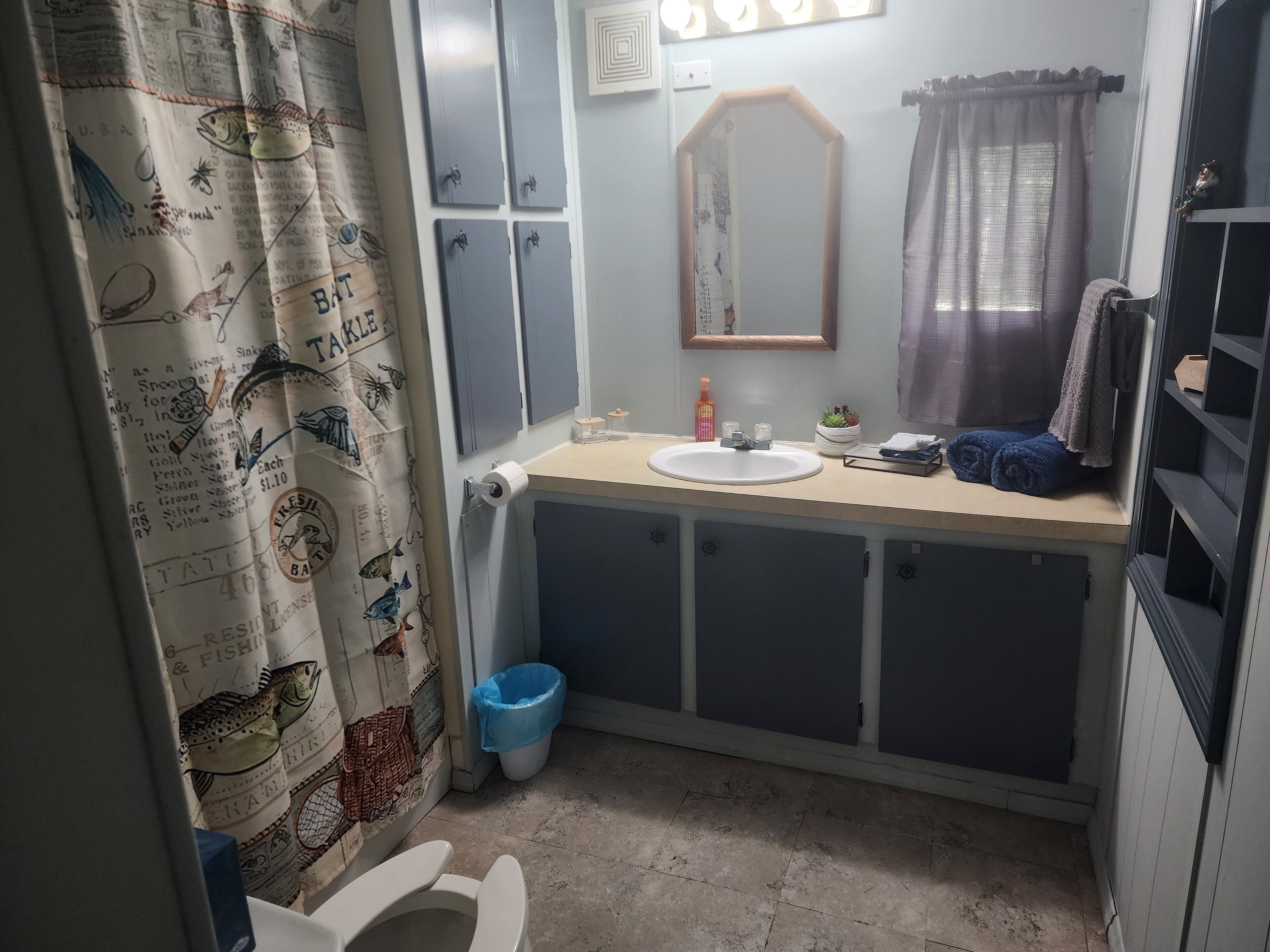 Ein Badezimmer mit Toilette, Waschbecken, Spiegel und einer blauen Mülleimer.