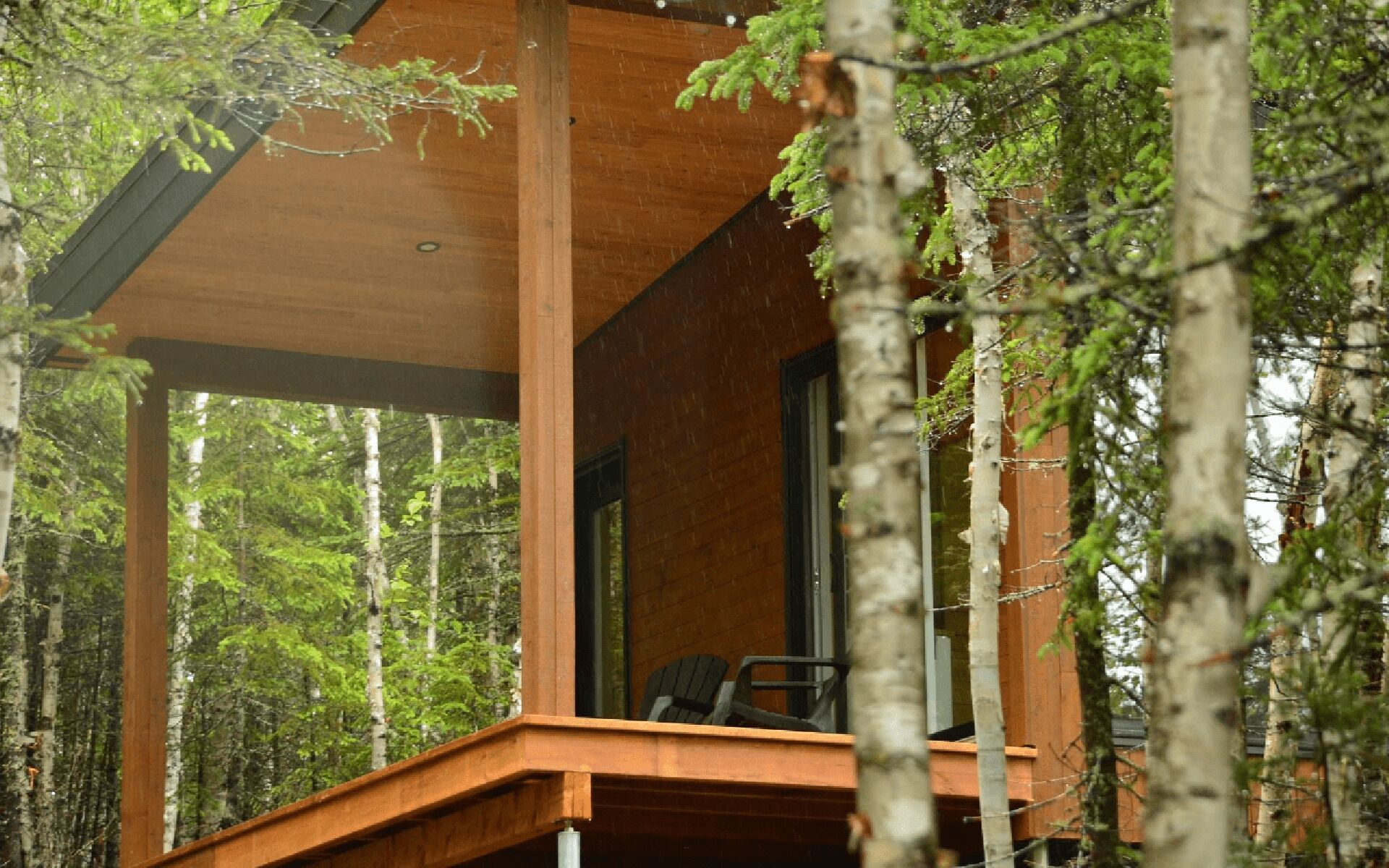 A wooden cabin with a balcony, surrounded by tall trees.