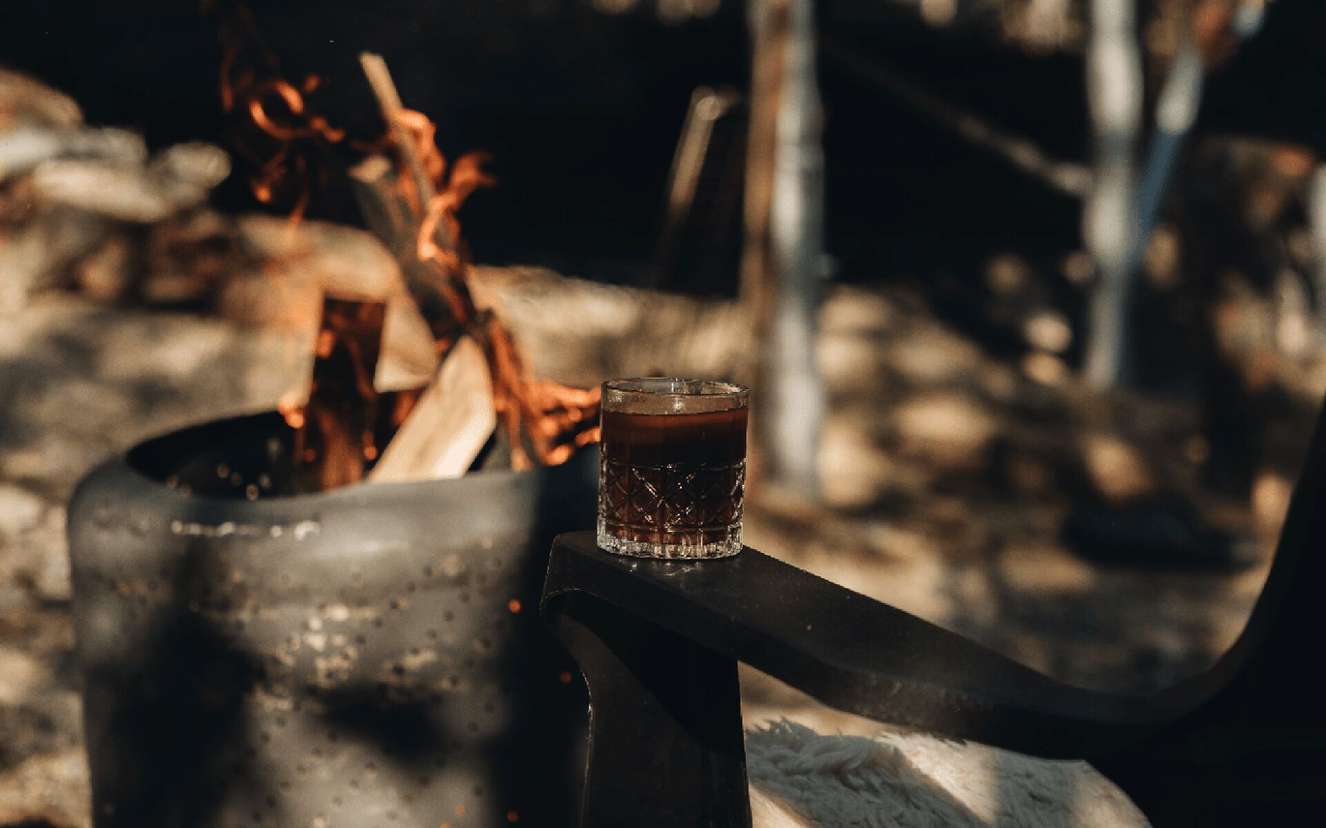 A close-up of a metal container with a glass of liquid, possibly a beverage, next to a fire.