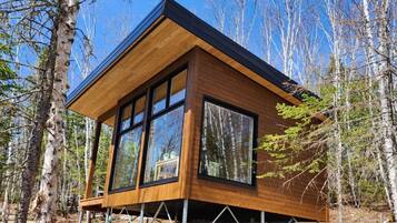 Eine moderne Holzhütte mit großen Fenstern, umgeben von Bäumen.