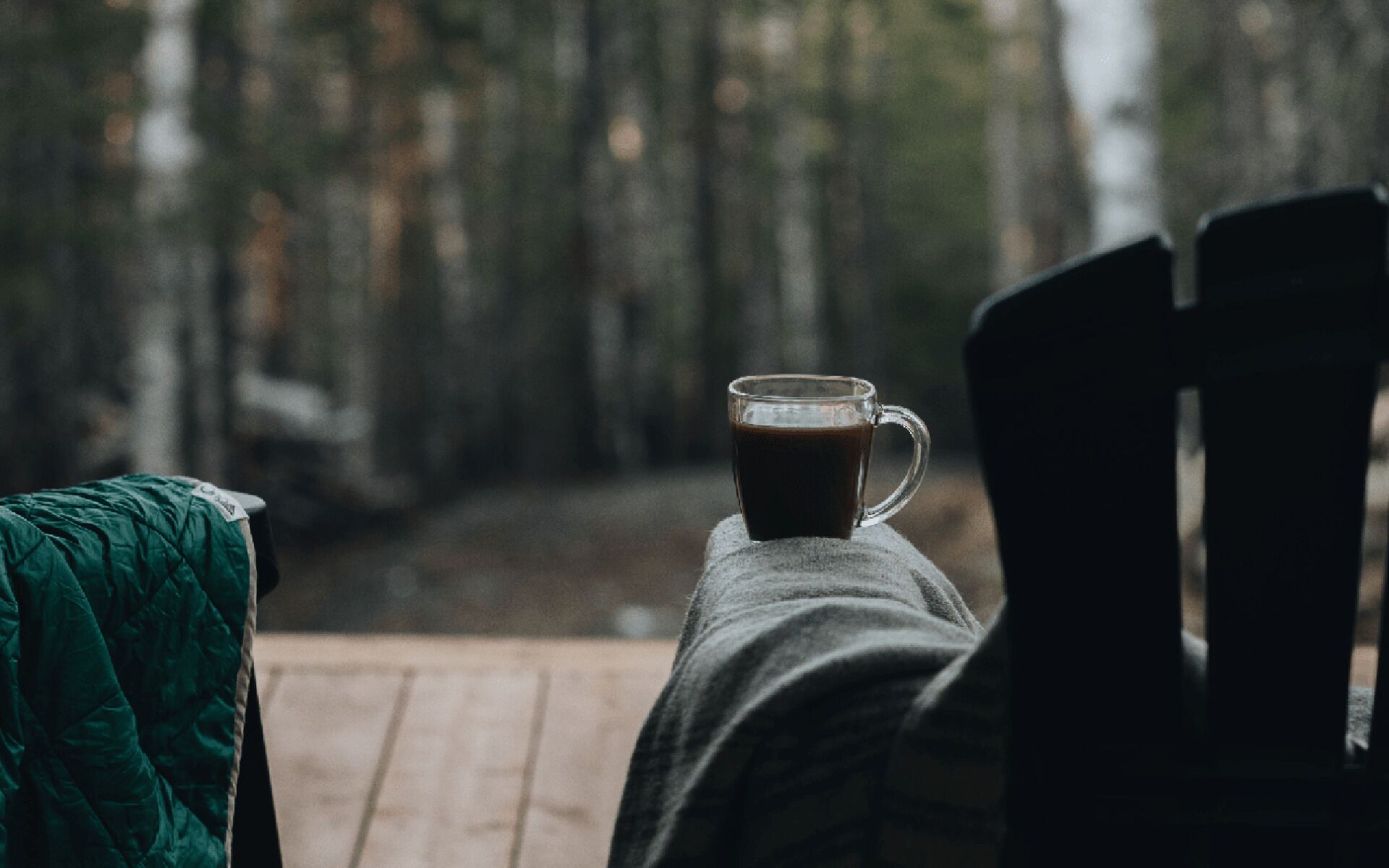 A wooden deck with a glass of coffee and a green blanket.