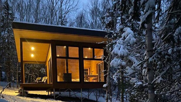 Una cabaña moderna con ventanas amplias, chimenea y una terraza.