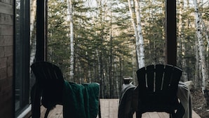 Una terraza de madera con dos sillas Adirondack mirando hacia un bosque.