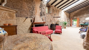 A rustic stone interior with a fireplace, red seating, and a view to the outside. - 'Ca'n Pont' with Mountain Views, Private Pool and Wi-Fi (Illes Balears)