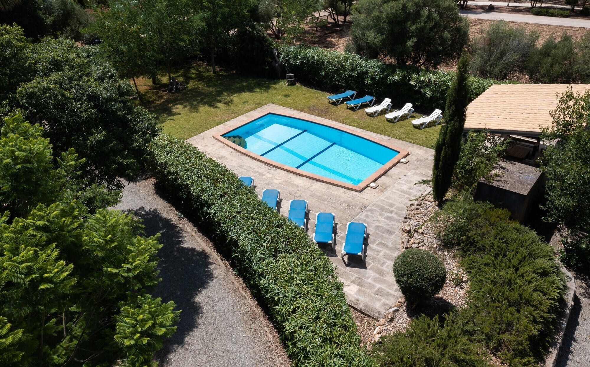 Vue aérienne d’une piscine entourée de chaises longues, de verdure et d’une terrasse en pierre.