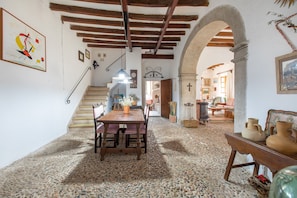 A rustic interior with a wooden staircase, a dining area with a table and chairs, and a living room with a sofa and decorative items.