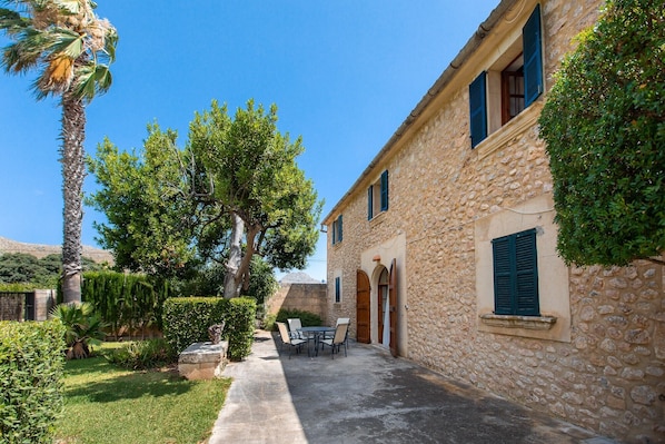 A stone building with a courtyard, a palm tree, and a table with chairs.