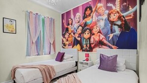 A bedroom with two single beds, a large mural of animated characters, and a nightstand with a lamp.