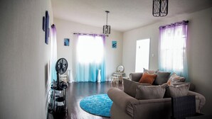 Un salon avec un canapé, un ventilateur, une petite table et un tapis bleu.