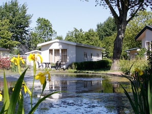Ein weißer Wohnwagen mit einer kleinen Terrasse und einem Teich davor.