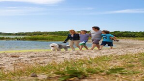 A family walking along a sandy beach with a dog, near a body of water and greenery in the background. - Nice Safari Tent Near Recreation Area (Noord-Scharwoude)