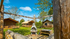 A rustic outdoor seating area with a fire pit, wooden deck, and cabins in the background. - Nice Safari Tent Near Recreation Area (Noord-Scharwoude)
