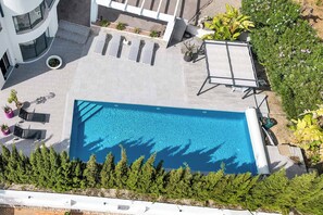 Vue aérienne d’un espace piscine comprenant une piscine moderne, des chaises longues et un patio avec des sièges.