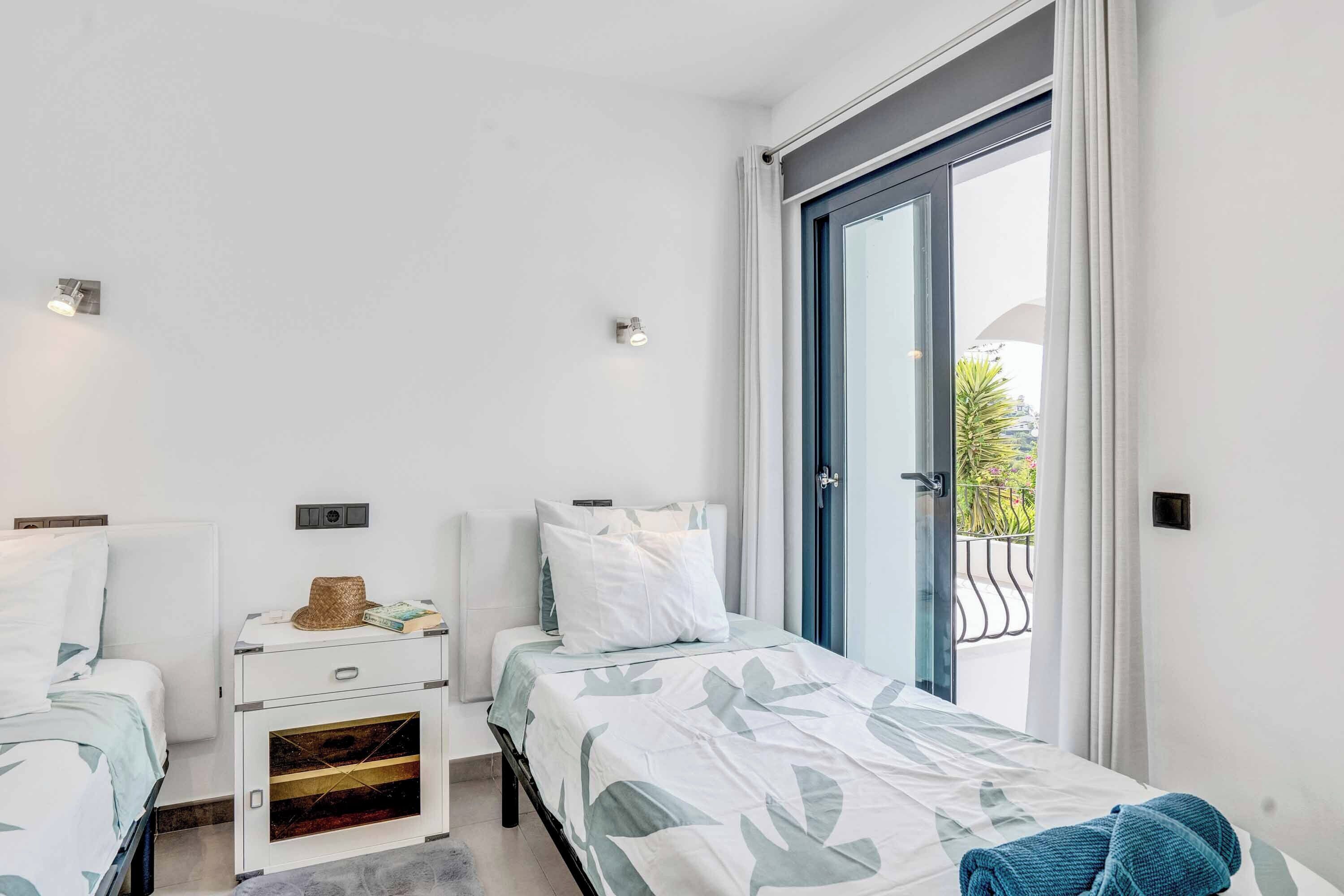 A modern bedroom with a bed, bedside tables, and a window with a view of the outdoors.