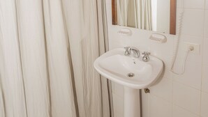 A bathroom with a white sink, a mirror, a hairdryer, and a shower curtain.