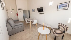 A modern living room with a grey sofa, a striped armchair, a dining table with chairs, a small white table, a mounted TV, and a framed picture on the wall.