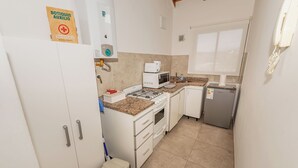 A compact kitchen with white cabinets, a microwave, a small refrigerator, and a gas stove.