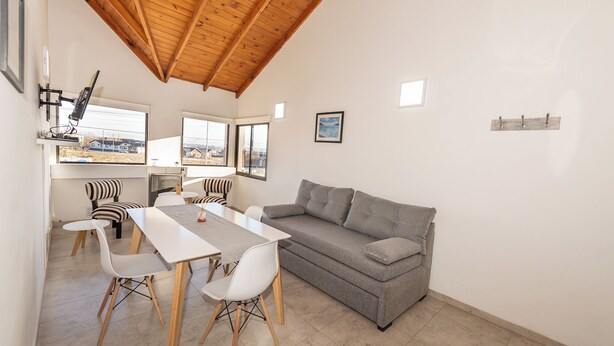 A modern living room with a dining area, a grey sofa, and a wooden ceiling.