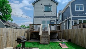 A backyard with a wooden deck, a barbecue grill, a fire pit, and a small American flag.