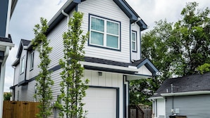 A two-story residential house with a garage, a small front yard with two young trees, and a wooden fence.