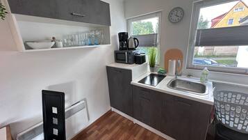 Een kleine keuken met een spoelbak, een koffiezetapparaat en een klok aan de muur.