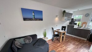 Ein modernes Wohnzimmer mit einem dunkelgrauen Sofa, einem kleinen Esstisch und einer Küchenzeile mit Mikrowelle und Kaffeemaschine.