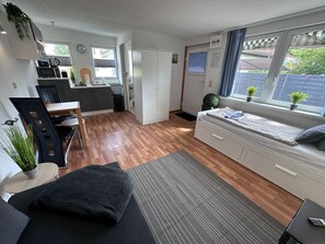 A compact living space with a kitchenette, a dining area, a bed with a window seat, and a small balcony with plants.
