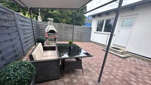 Eine Terrasse mit einem Glastisch, Korbmöbeln und einem Steinofen.