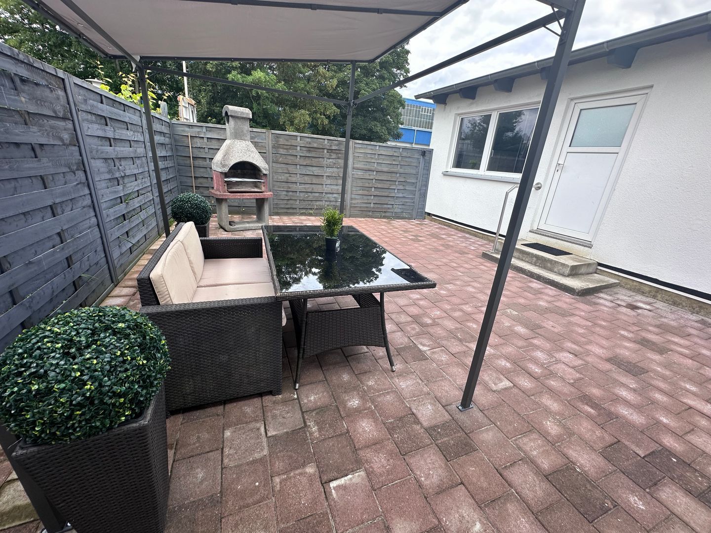 A patio area with a glass-top table, wicker furniture, and a stone oven.
