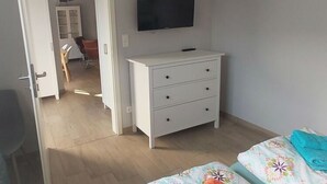 Een slaapkamer met een bed, een aan de muur bevestigde televisie en een witte dressoir.