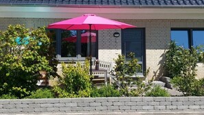 Een huis met een pannendak, een bakstenen gevel en een roze paraplu ervoor.